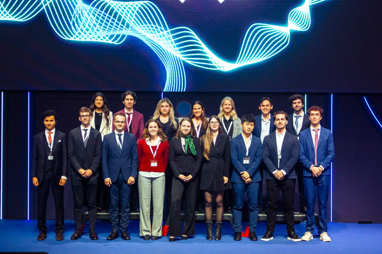 A university group photograph on stage under blue lighting